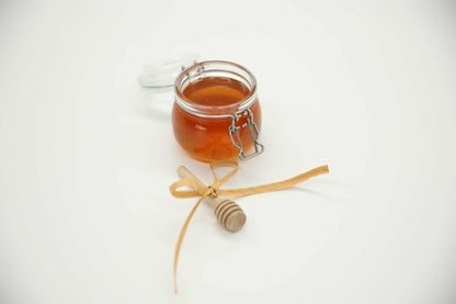 Wooden honey dipper drizzling raw honey — controlled pour from Beeline Organic honey jar