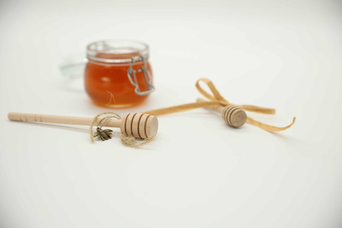Wooden honey dipper stick in raw honey jar — grooved head captures and drizzles honey evenly